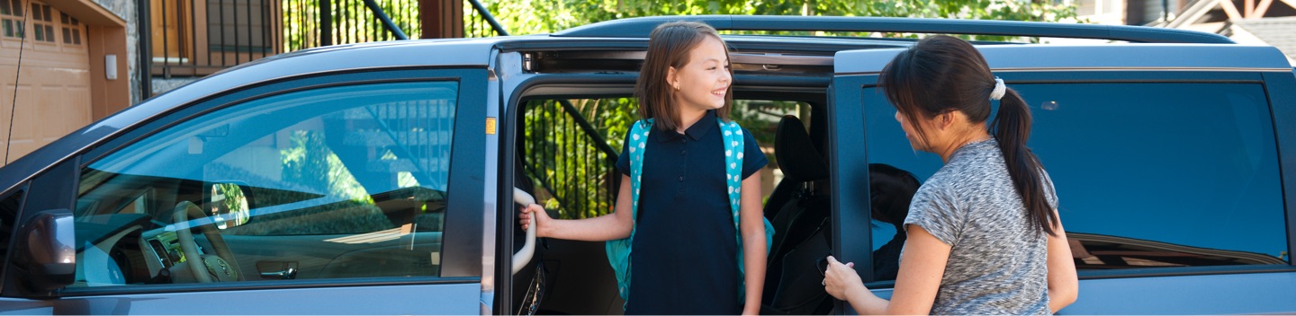 Young Girl Wearing Backpack Standing In Doorway Of Van With Mother Nearby