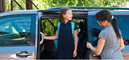 Young Girl Wearing Backpack Standing In Doorway Of Van With Mother Nearby